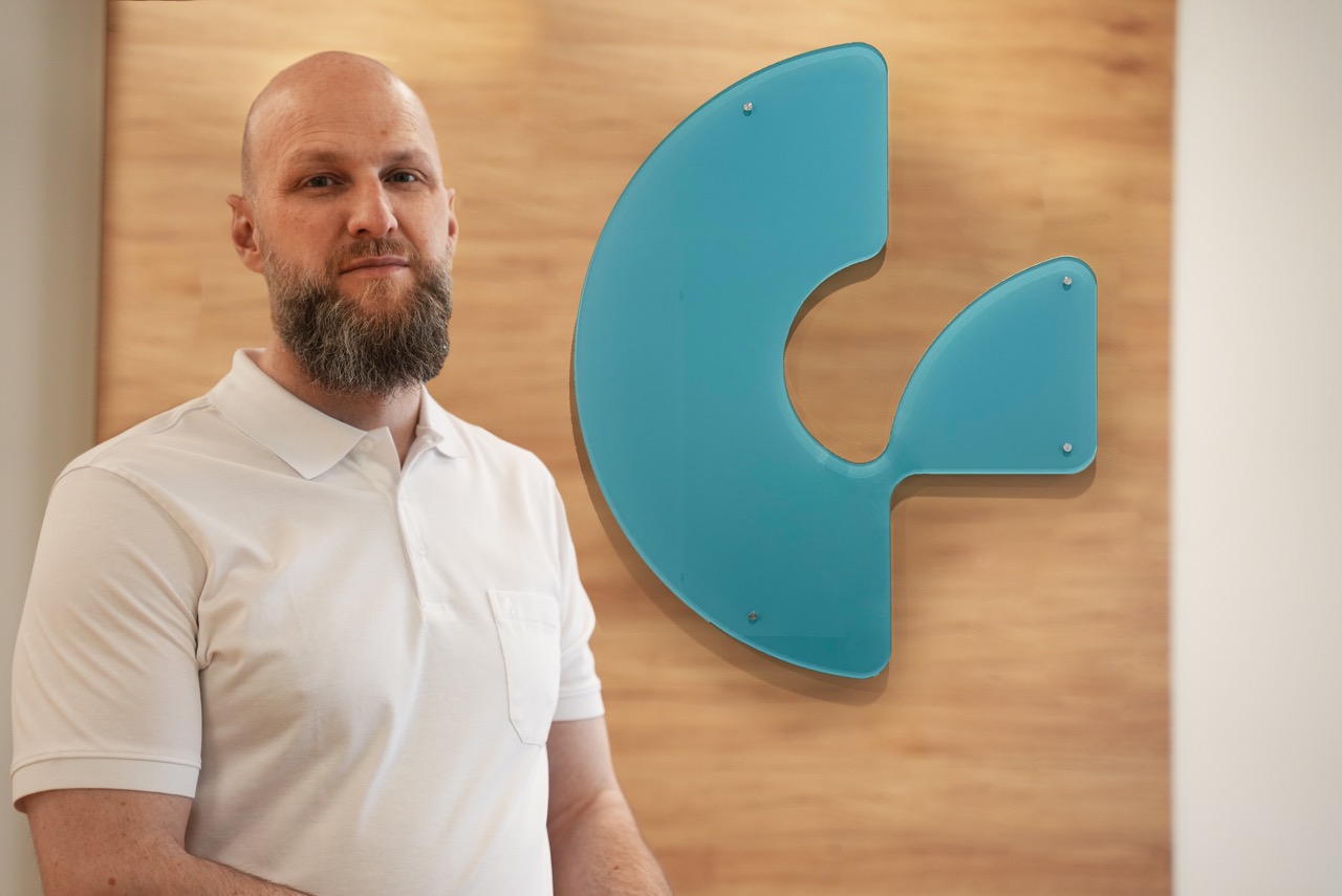 Dr. Gröbner in der Ordination neben dem Praxis-Logo